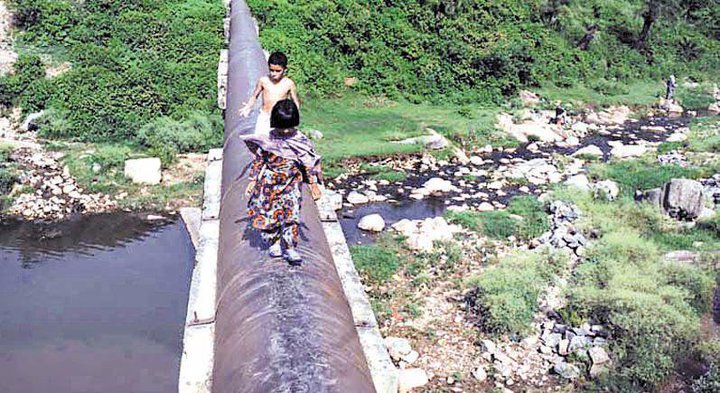 2 kids crossing water by small gas pipe line